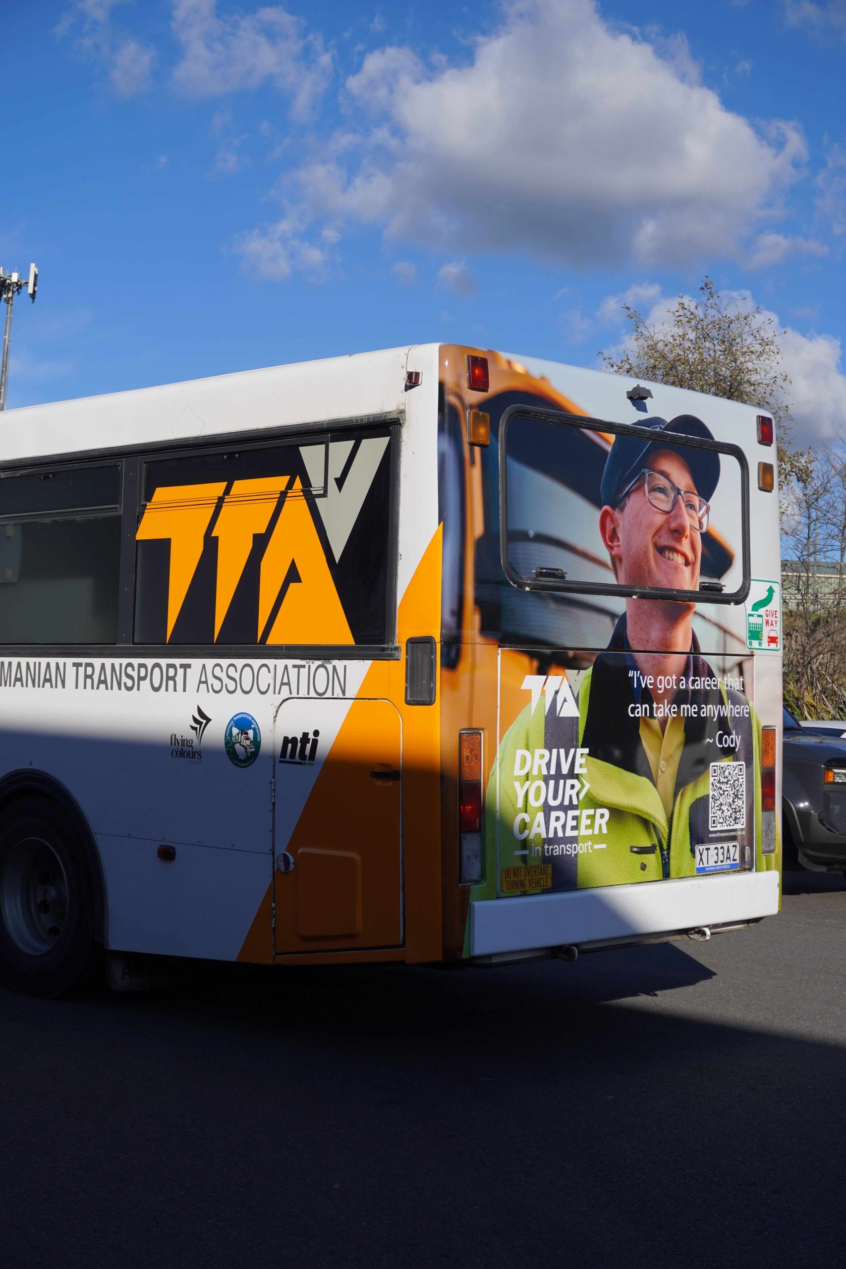 TTA Bus Wrap Side Profile Tasmanian Transport Association bus wrap installed by Flying Colours Group featuring bold orange and white branding.