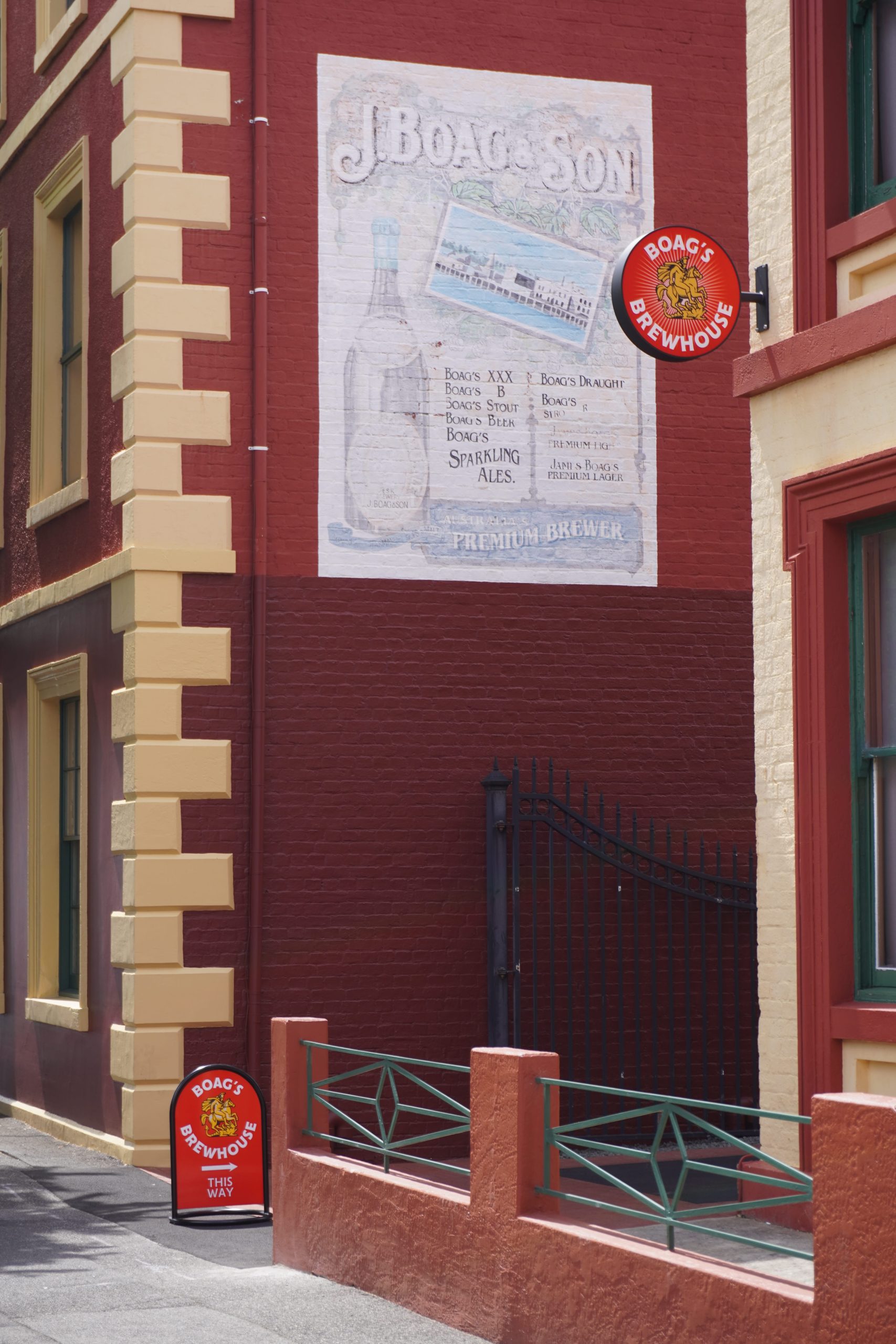 Round red Boag’s Brewhouse sign beside a heritage brewery mural, with a directional pavement sign below.
