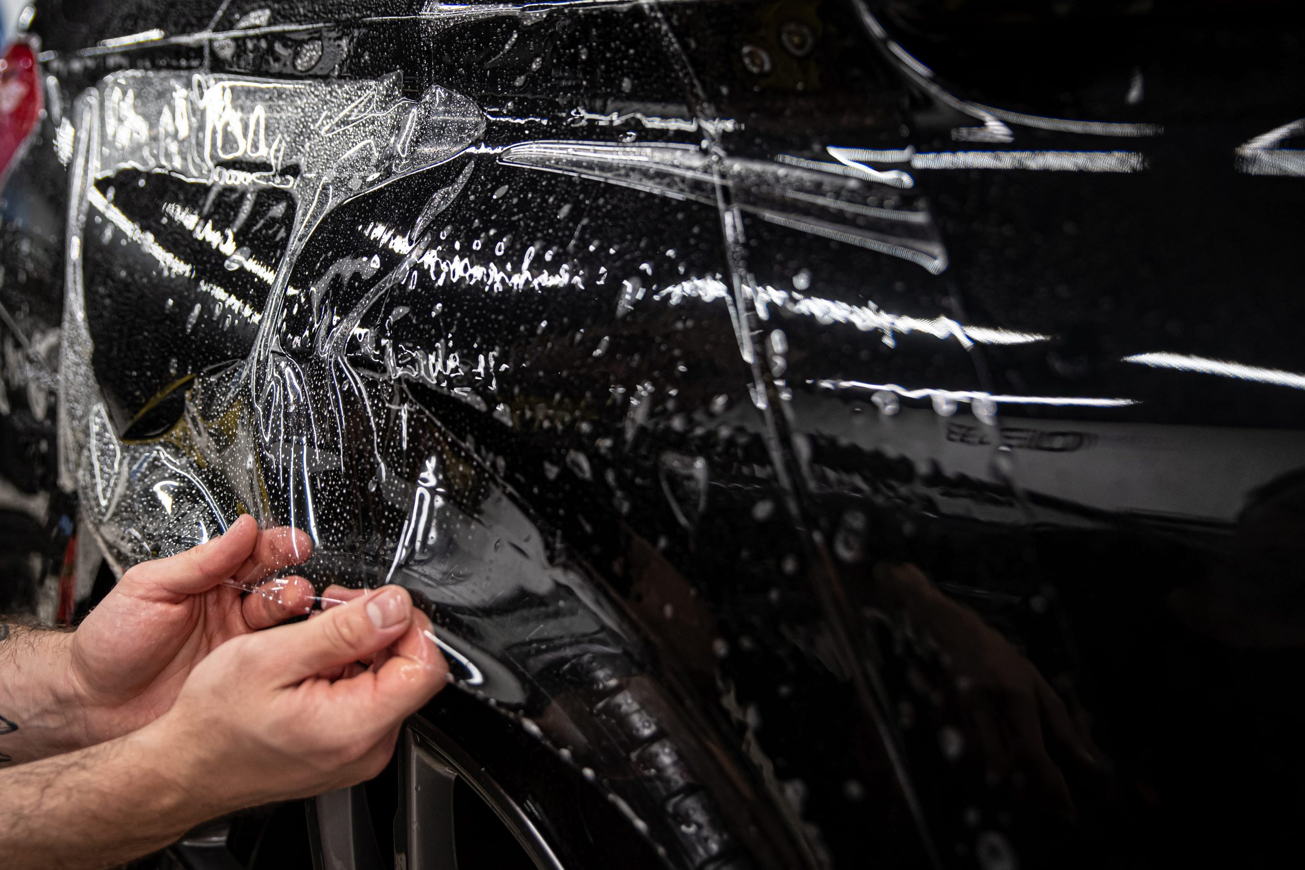 Paint Protection Film Fitting – Wheel Arch Installer positioning clear paint protection film around the wheel arch of a black vehicle.